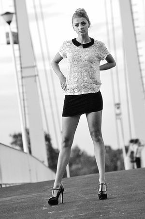 Young model in pencil mini skirt, lace shirt and t strap heels on a bridge.