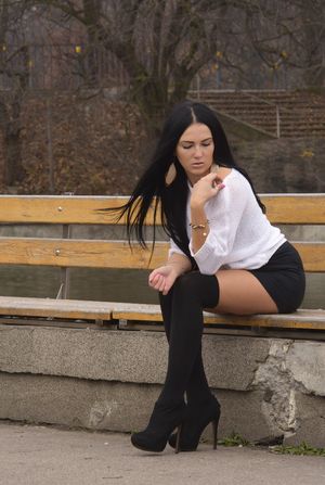 Cute brunette in black knee-highs and white sweater in a park.