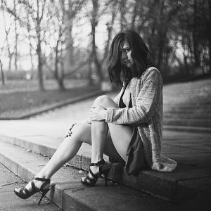 Slim brunette sitting on a stairs in the park just in heeled sandals and coat