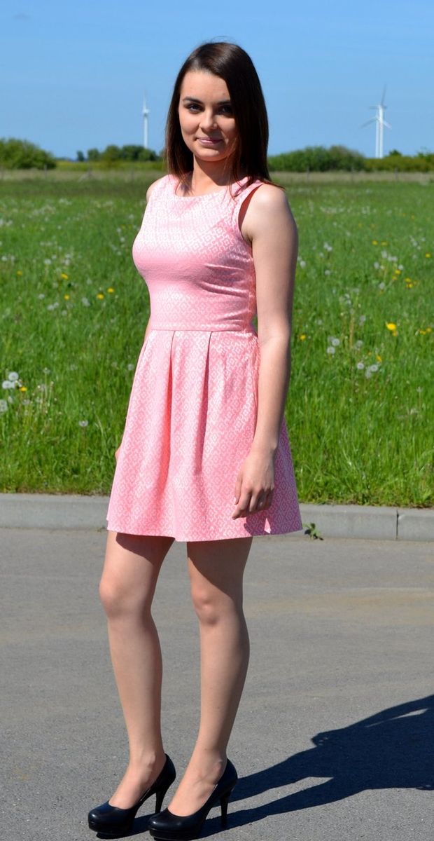 Young brunette posing in cute pink dress on the road outdoors