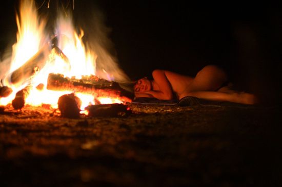 Sexy woman naps nude by the campfire at night