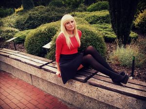 Nice blonde girl posing outdoors in black skirt, stockings, heels and sheer red top