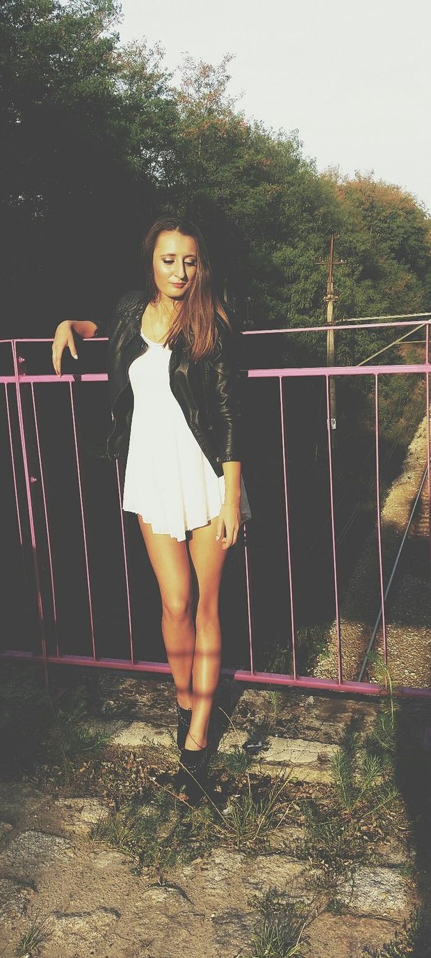 Leggy chick in short dress and leather jacket posing outdoors