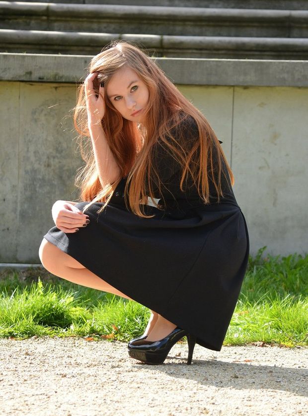 Young redhead hottie posing outdoors in shiny high heels and black dress