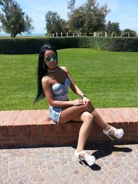 Tanned bimbo in slutty outfit and white high heels posing outdoors