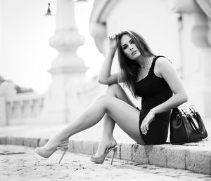 Leggy model in tight mini black dress and high heels on the street at black and white photo