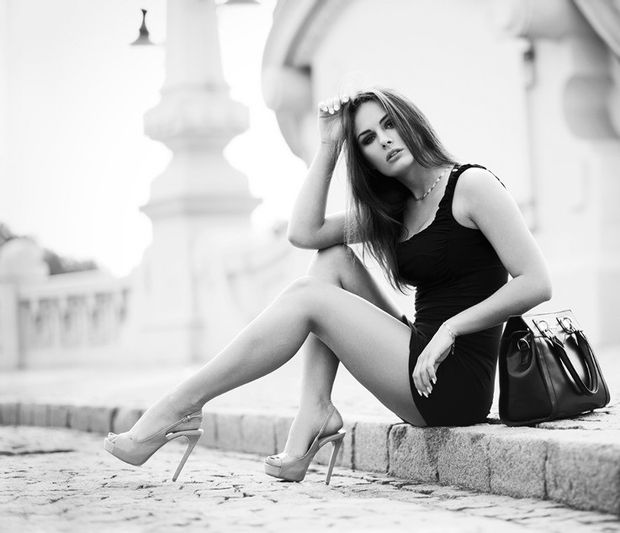Leggy model in tight mini black dress and high heels on the street at black and white photo