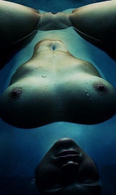 Interesting nude photograph aquatic blue floating on back with boobs and face above surface pussy submerged with moon lighting effect.