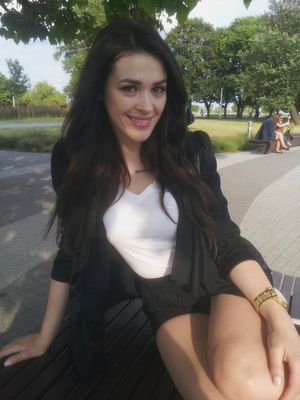 Lovely brunette wearing black shorts and jacket, sitting on a bench in the park