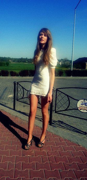Slim blonde posing outdoors in white derss and heeled sandals