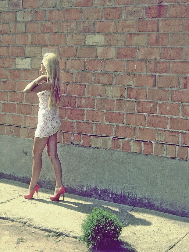 Blonde bimbo posing outdoors in red high heels and lace dress
