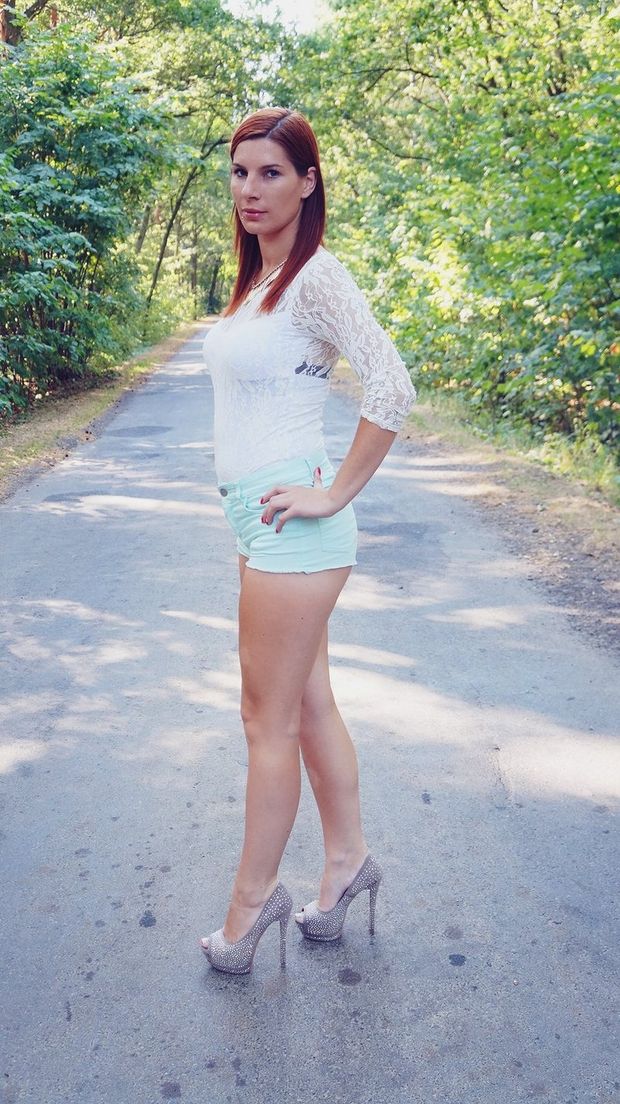 Tall and leggy redhead posing outdoors in white lace bluse and shorts