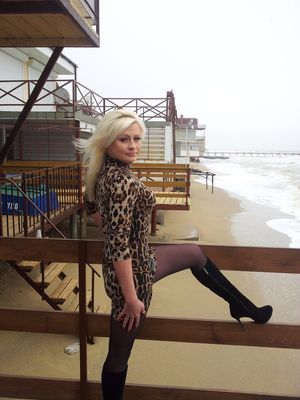 Blonde bimbo in tight mini dress and black heeled boots outdoors