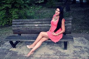 Dark hair leggy chick sitting on a bench in a apark