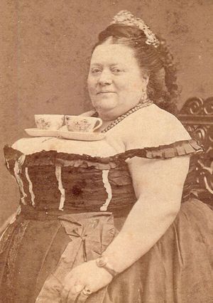 Victorian woman balancing tea cups on her chest.