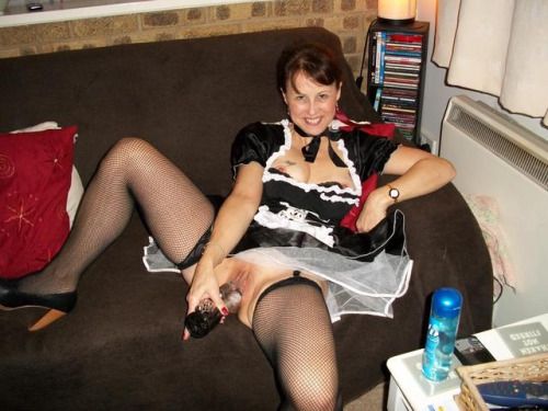 Smiling woman in sexy dress pushes the dildo into the cunt