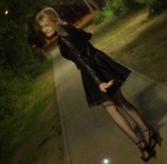 Sexy insta chick posing outdoors in short mini skirt, leather jacket high heeled sandals and nylons