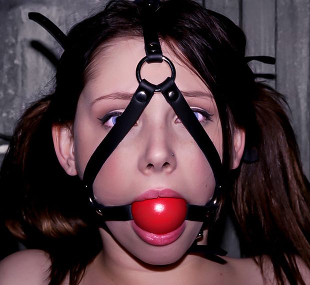 Bright eyed teen with pig tails silenced by a huge red ballgag that's secured tightly in her mouth