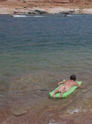 nude male floating on lake with boats in background