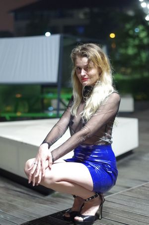 Hot blonde model posing in sheer blouse and micro latex skirt outdoors braless