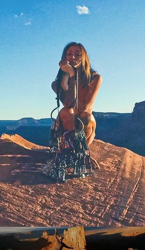Nude rock climber squats behind her rack