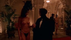 A masked couple in the background share a kiss through their masks while walking to the pleasure rooms - Eyes Wide Shut orgy