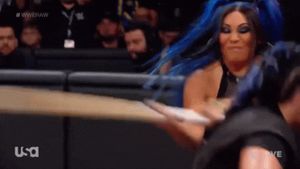 Mia Yim hitting Rhea Ripley with a kendo stick.