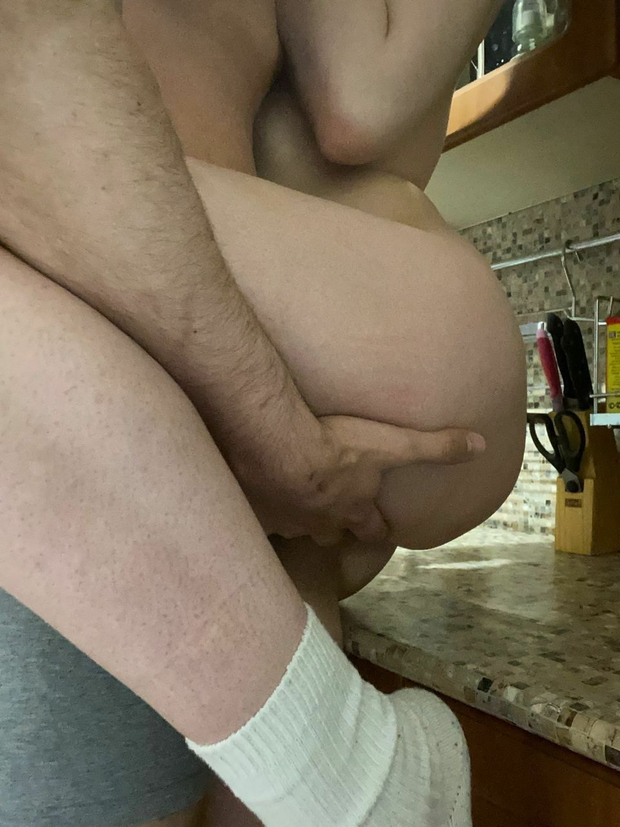 He grabs her ass and pussy from below as she leans/sits on the kitchen counter