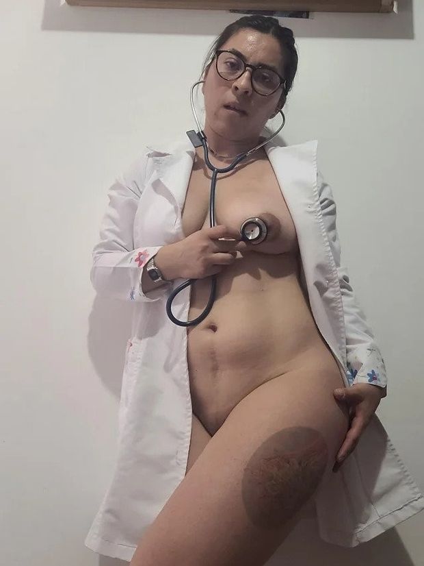 Nurse in lab coat listening to her heartbeat with a stethoscope.