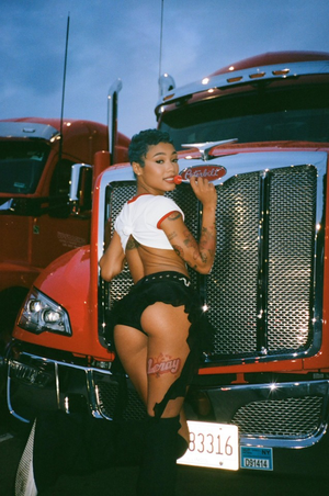 Coi Leray posing in front a truck with a lollipop.
